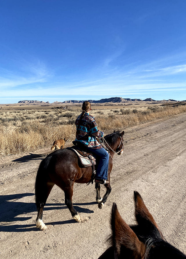 Back view of a woman riding a horse in Aztec blue brown fleece jacket
