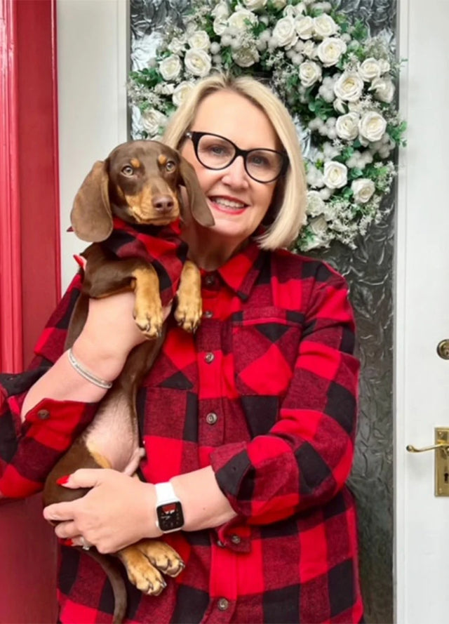 A lady in a red flannel shirt holding a dog in cute flannel bandana