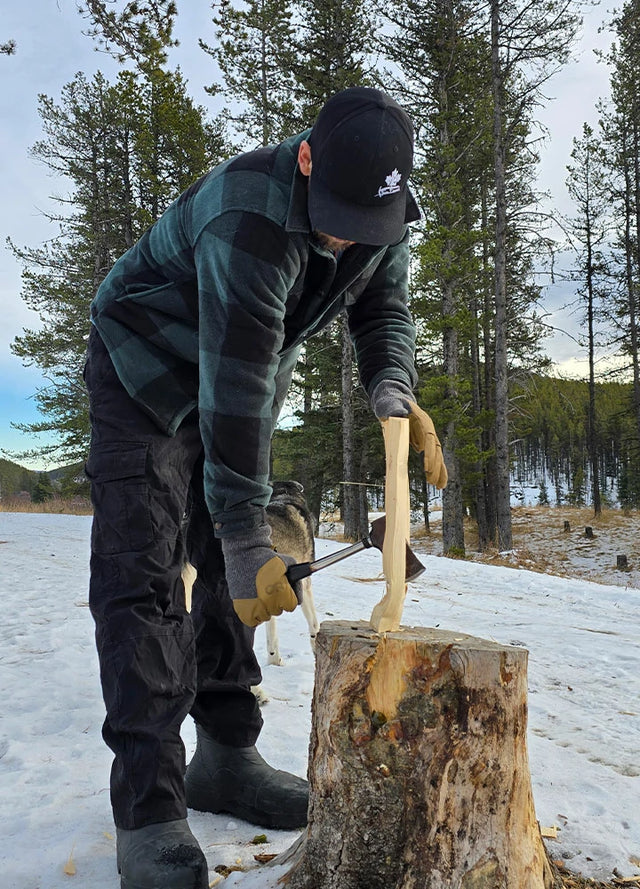 Front view of a man in a black green men's cozy plaid sherpa lined shirt jacket is chopping wood