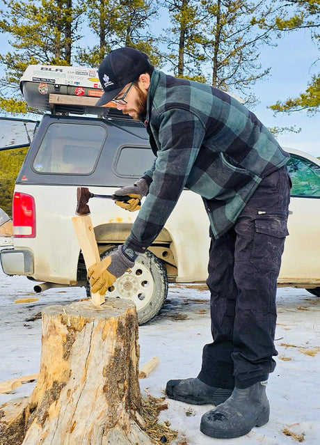 Side view of a man in a black green men's cozy plaid sherpa lined shirt jacket, chopping wood