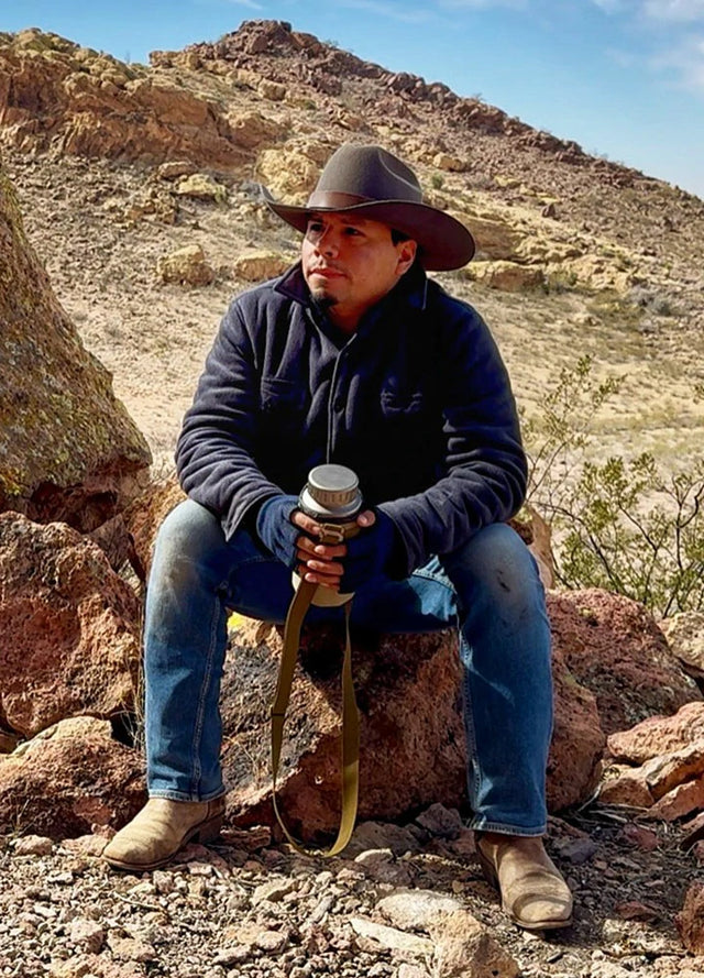 Front view of a man in a twill grey men's warm sherpa lined fleece shirt jacket sitting on a rock