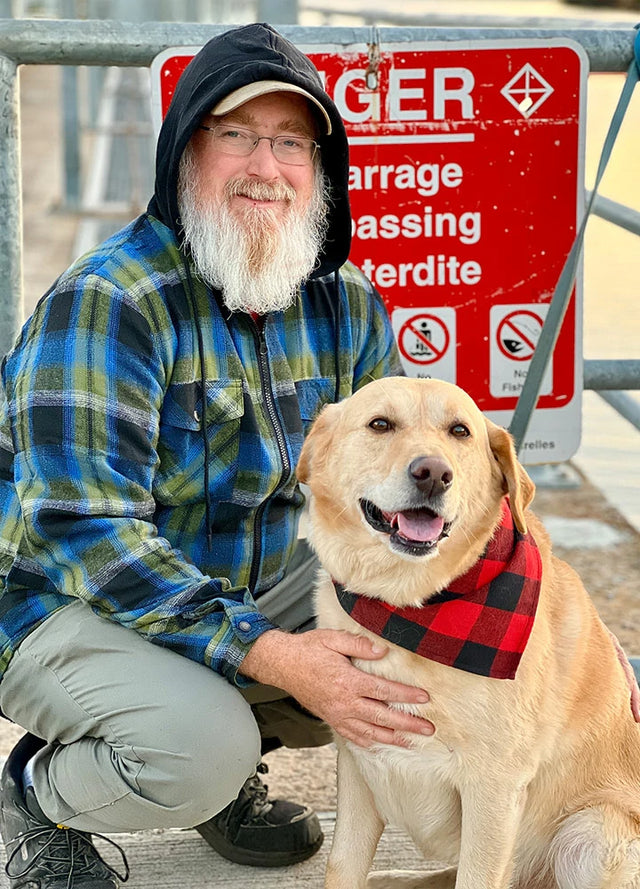 Front view of a man in green blue men's sherpa lined flannel jacket with a hood holding a dog