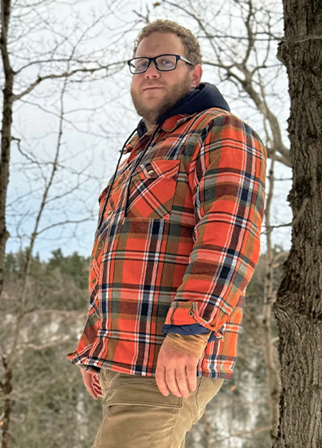 Side view of a man in an orange quilted lined plaid flannel shacket for men standing in the woods
