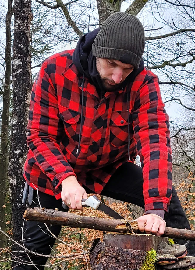 Front view of a man in a buffalo red black men's quilted lined plaid flannel shirt jacket sawing wood