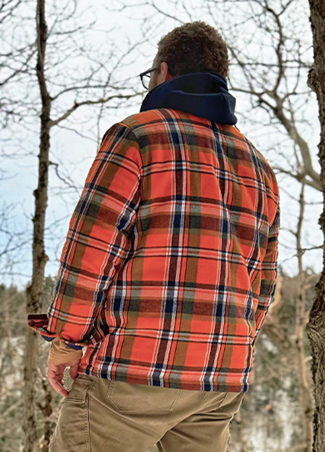 Back view of a man in an orange quilted lined plaid flannel shacket for men standing in the woods