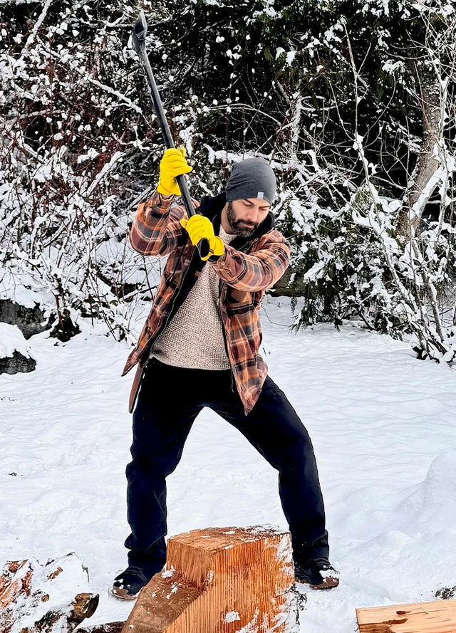 Front view of a man in a brown men's quilted lined flannel hooded jacket chopping wood