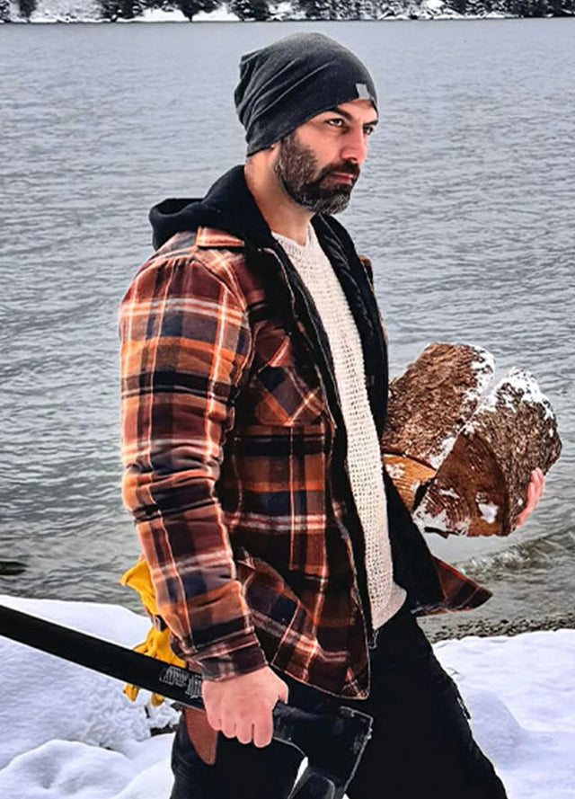 Side view of a man in brown men's quilted lined flannel jacket holding firewood and an axe in his hands