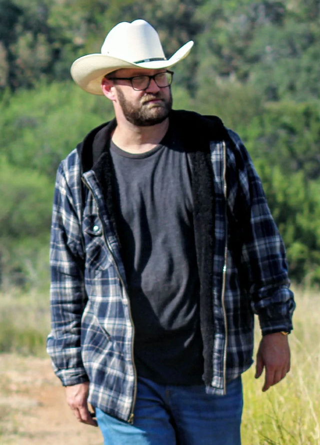 Front view of a man in a navy khaki men's plaid flannel hooded jacket walking in the grass