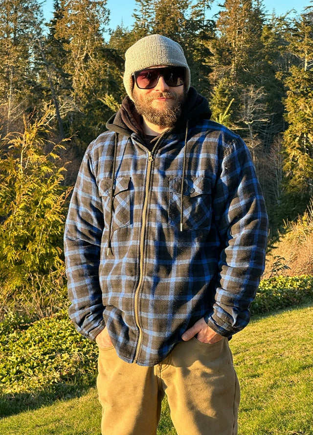 Front view of a man in a dark blue men's hooded flannel plaid jacket standing in the grass