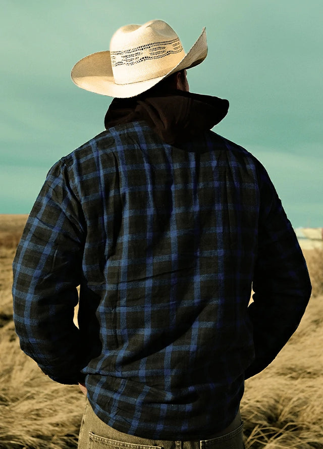 Front view of a man wearing a dark blue men's hooded flannel plaid jacket and leading his dog by the sea