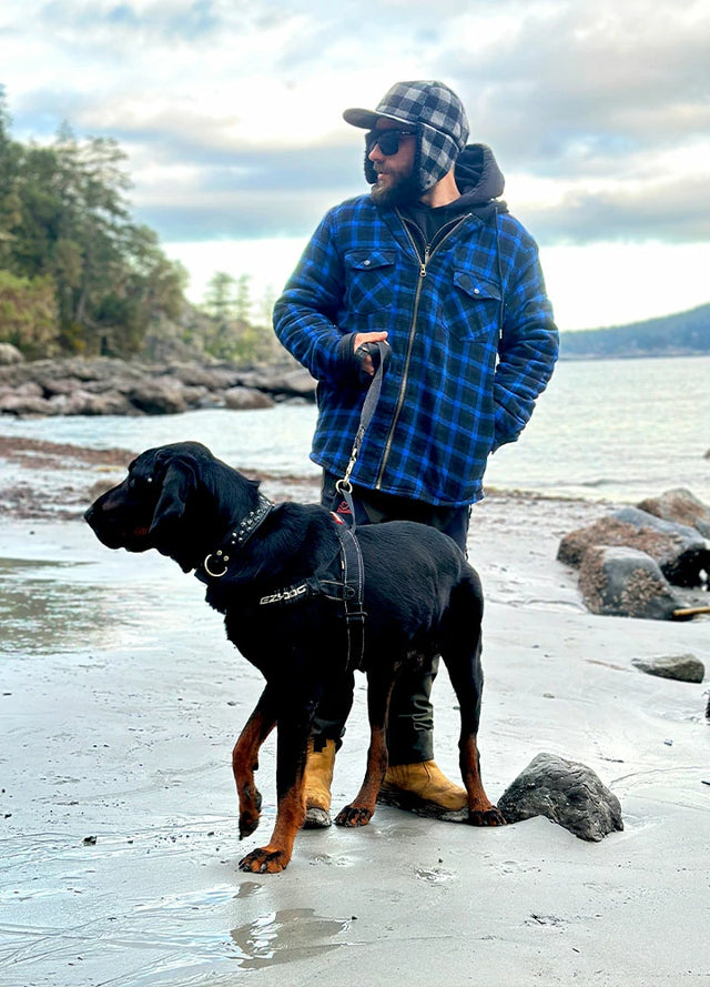 Front view of a man wearing a dark blue men's hooded flannel jacket leading his dog and looking to the side