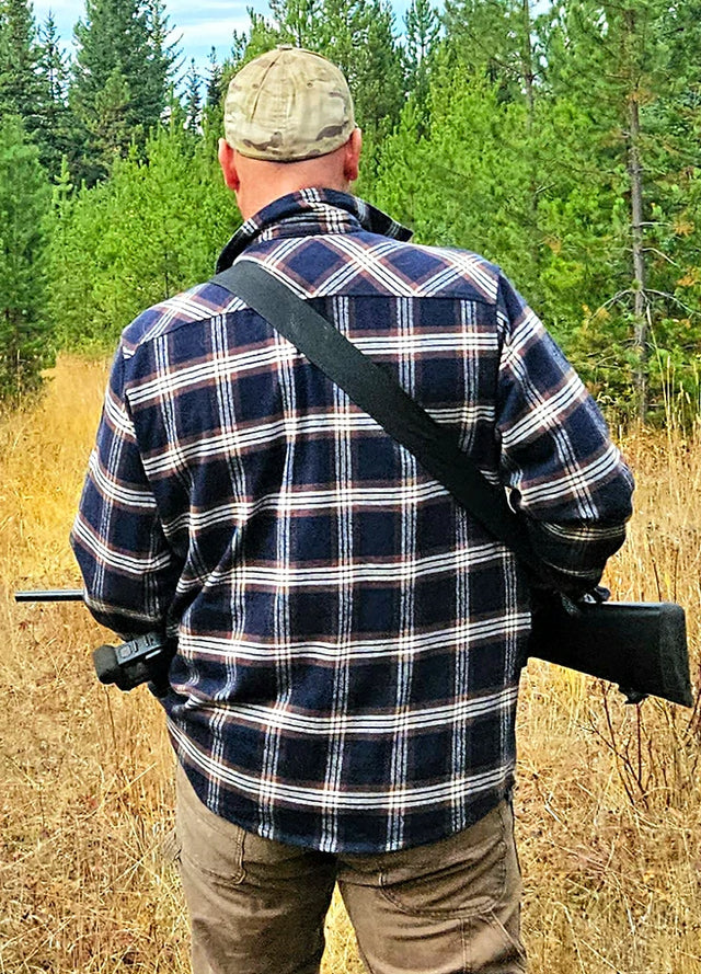 Back view of man wearing navy blue coffee men's durable flannel cotton shirt holding shotgun