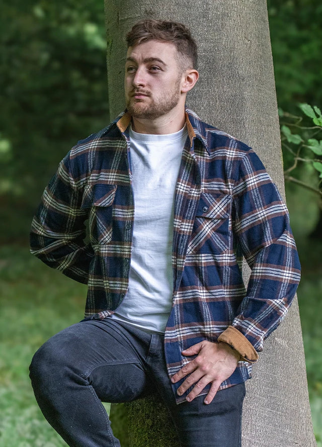 Front view of a man wearing a navy blue coffee men's durable flannel cotton shirt leaning against a tree