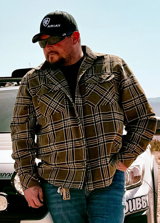 Front view of a man wearing a green men's flannel shirt watching the ground with one hand in his pocket