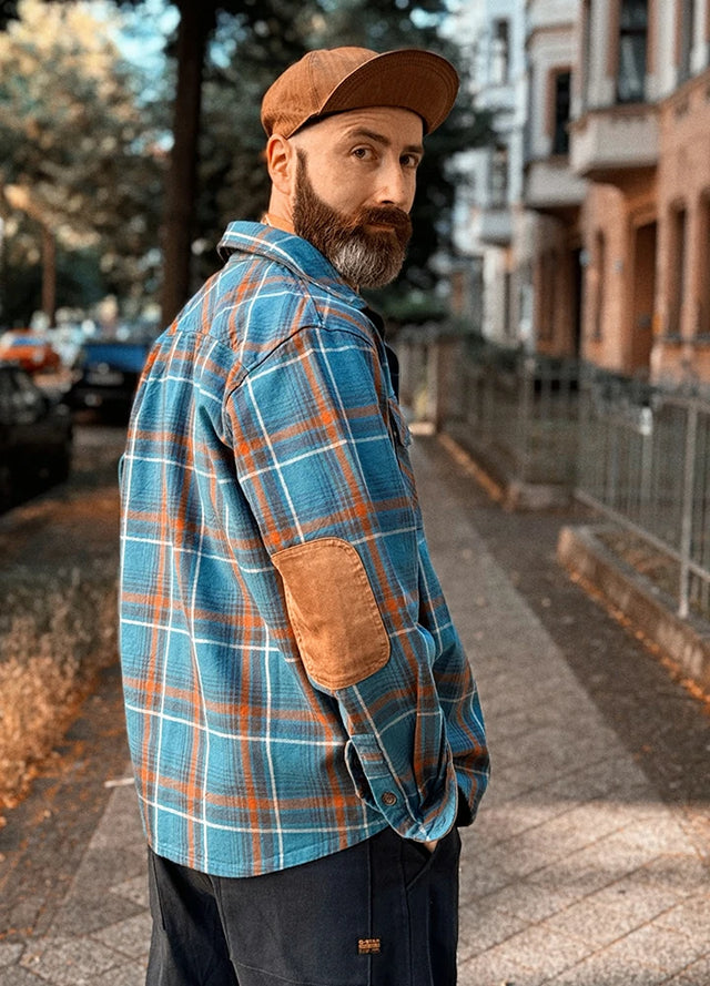 Back view of a man in a blue men's warm flannel plaid shirt with his hand in trouser pockets