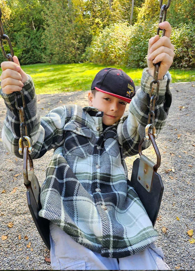 A young boy in a black-and-white checkered fleece jacket enjoys a moment on the swing