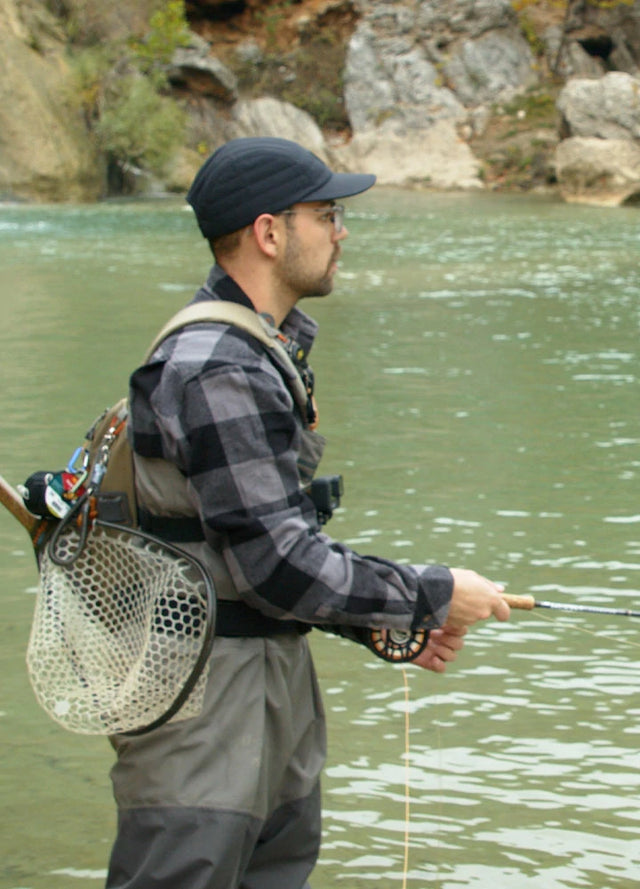 Side view of man in gray men's heavy cotton checkered shirt standing in water and fishing