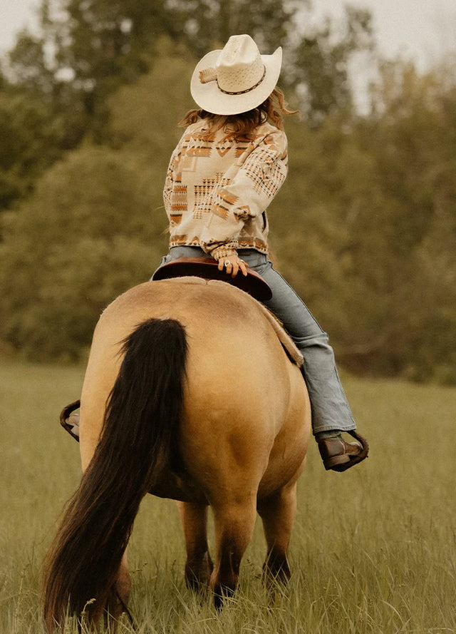 Back view of a woman on horseback wearing a khaki brown aztec lapel cropped jacket