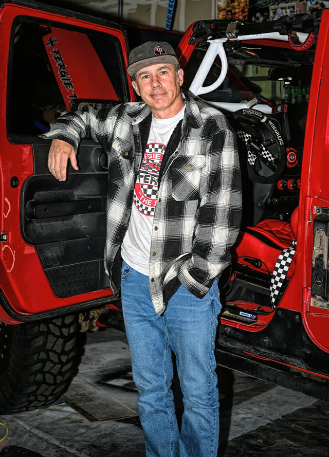 Front view of a man in a black white men's cozy snap button flannel shirt jacket leaning against a car door