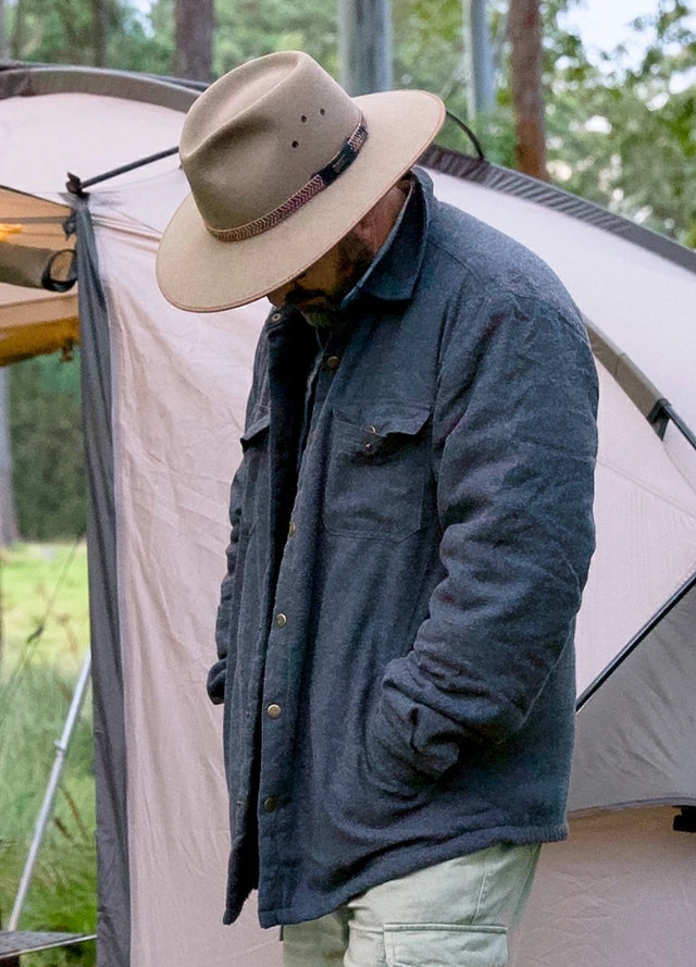Side view of a man in a dark gray men's sherpa lined plaid shirt jacket with his hands in the pockets