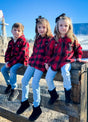 Children wearing red and black plaid flannel jackets sitting together enjoying the sunshine
