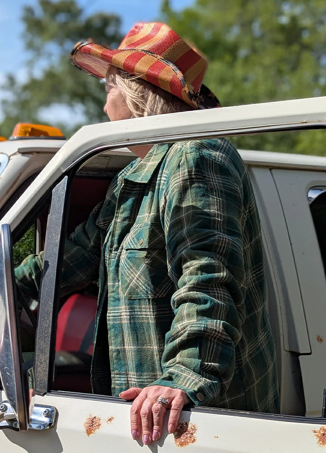 Side view of a woman in a green khaki full zip-up plaid jacket for men standing by the car door