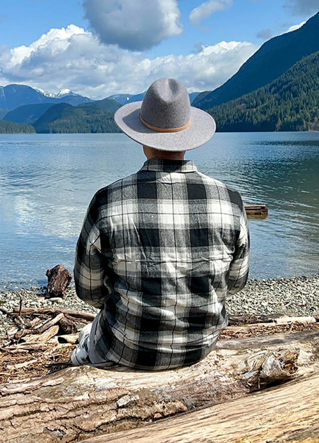Back view of a man in a white and black men's full zip-up plaid flannel jacket, wearing a hat