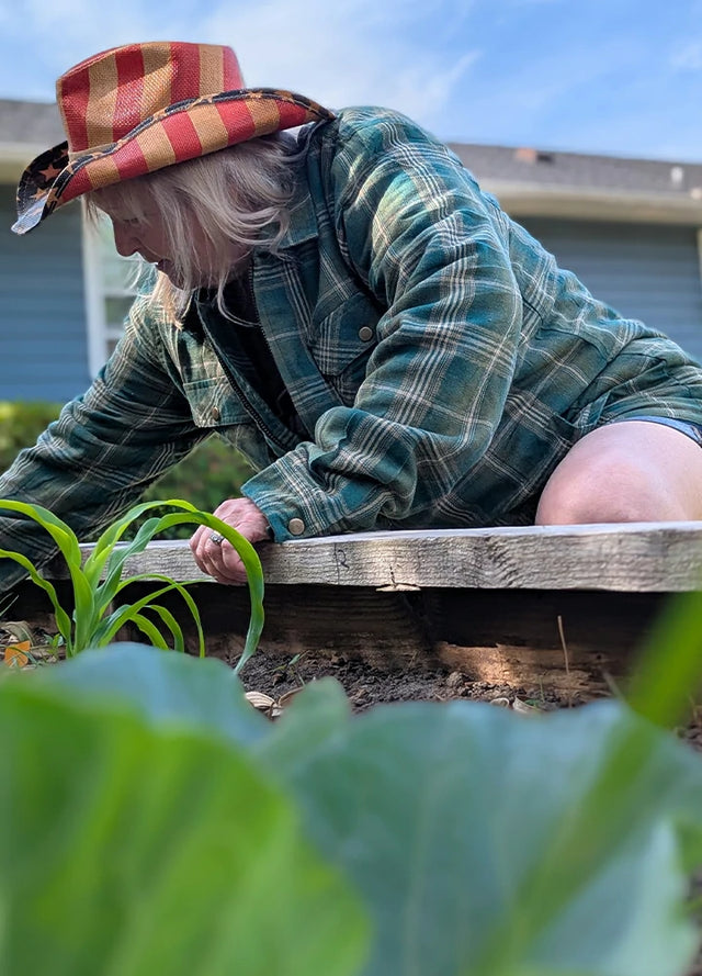 Side view of a woman in a green khaki full zip-up plaid jacket for men squatting in the vegetable garden