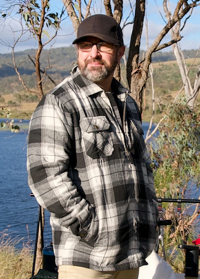 Front view of a man in a white and black men's full zip up plaid flannel jacket wearing a hat