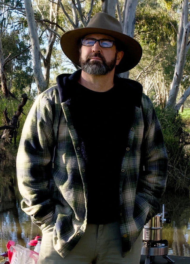 Front view of a man wearing a tea green men's hooded flannel jacket standing by a lake