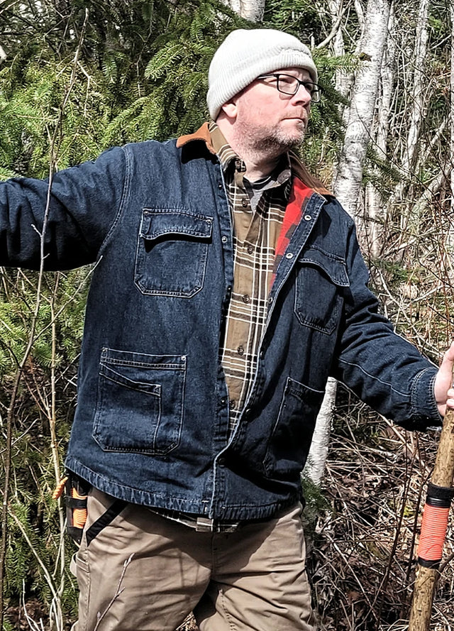 Side view of a man wearing an indigo men's flannel lined denim jacket standing in the woods