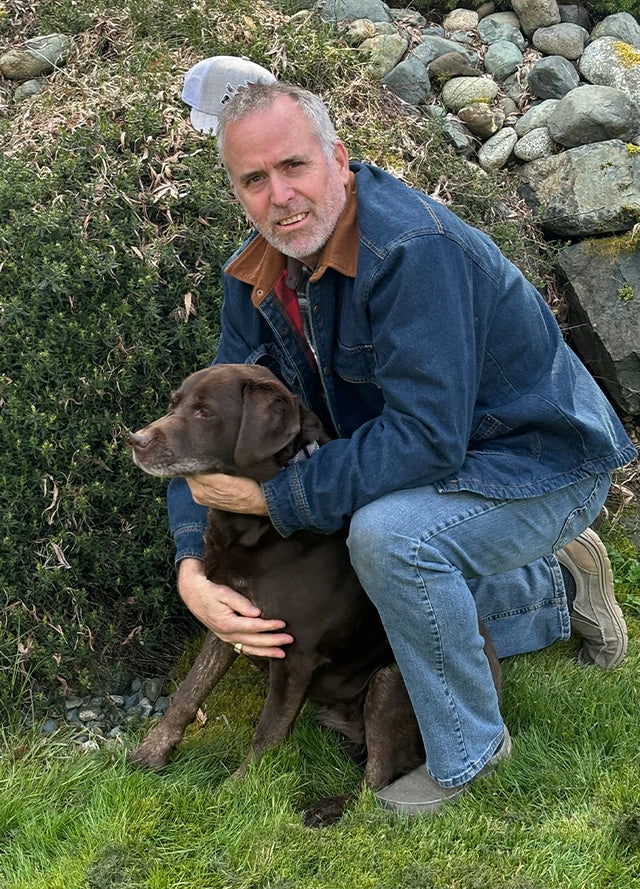 Side view of a man in an Indigo men's warm denim flannel lined shacket crouching on the grass