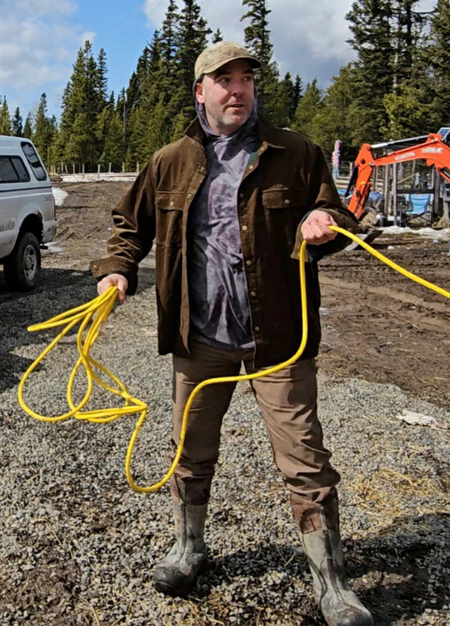 Front view of a man wearing a men's army green flannel-lined corduroy shirt jacket, working in a garden while holding a hose