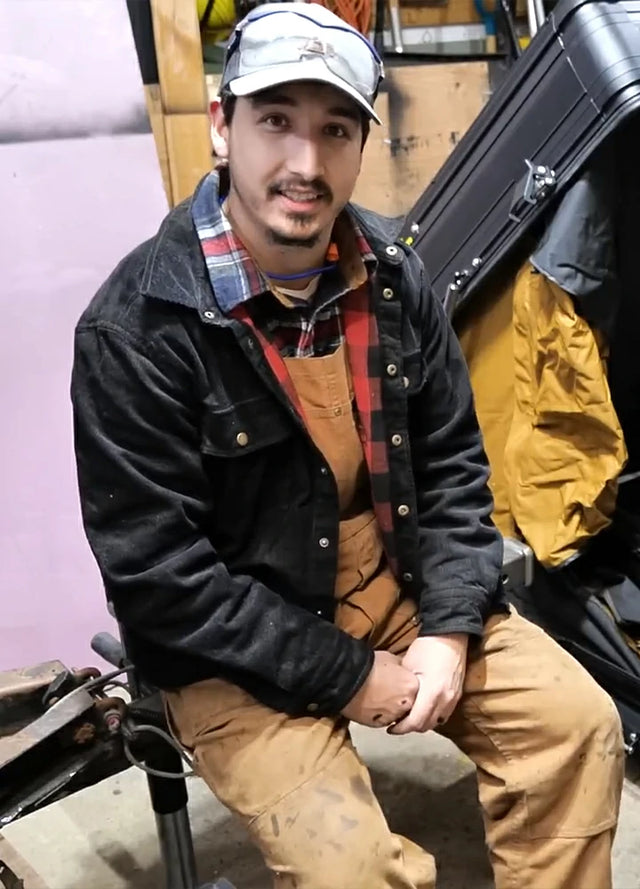 Front view of a man wearing a men's black flannel-lined corduroy shirt jacket, seated comfortably in a workshop