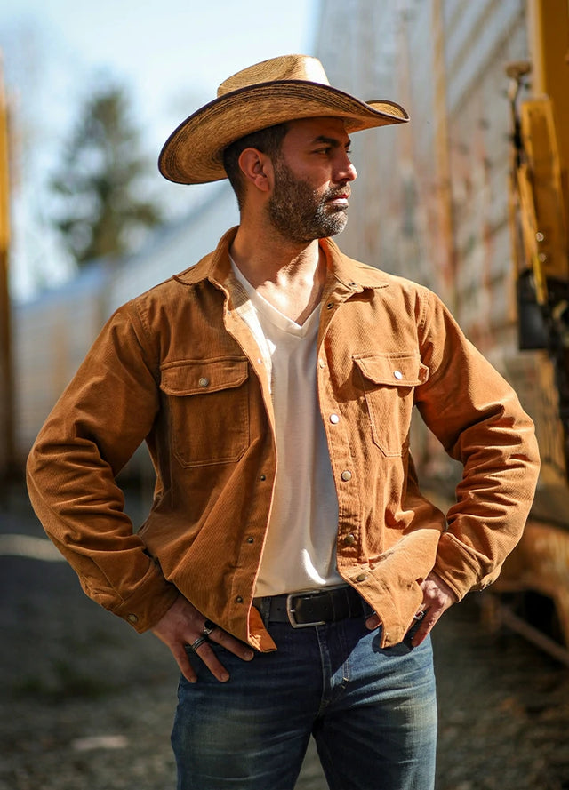 Side view of a man standing beside a train track with his hands on his hips, wearing a men's orange flannel-lined corduroy shirt jacket