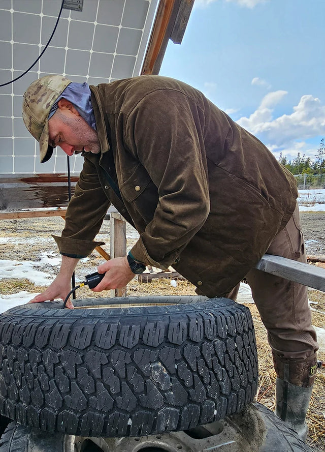Front view of a man wearing a men's army green flannel-lined corduroy shirt jacket, repairing a tire in a workshop