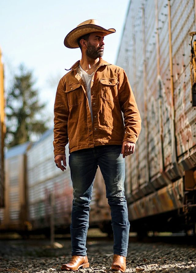 Front view of a man wearing a men's orange flannel-lined corduroy shirt jacket, standing beside a train platform