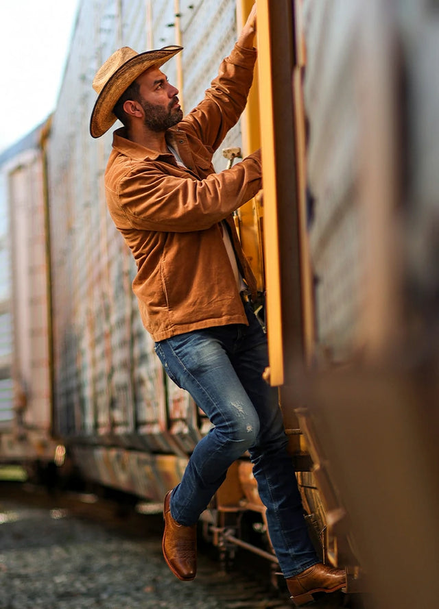 Side view of a man wearing a men's orange flannel-lined corduroy shirt jacket, holding onto the door frame of a train car