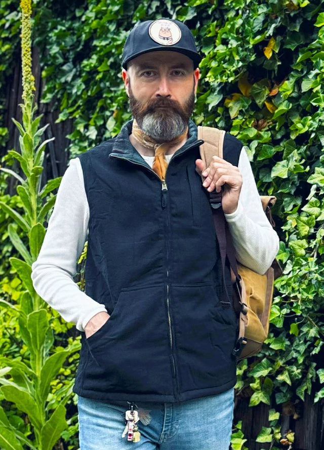 Front view of a man in a black green plaid men's reversible vest carrying a backpack