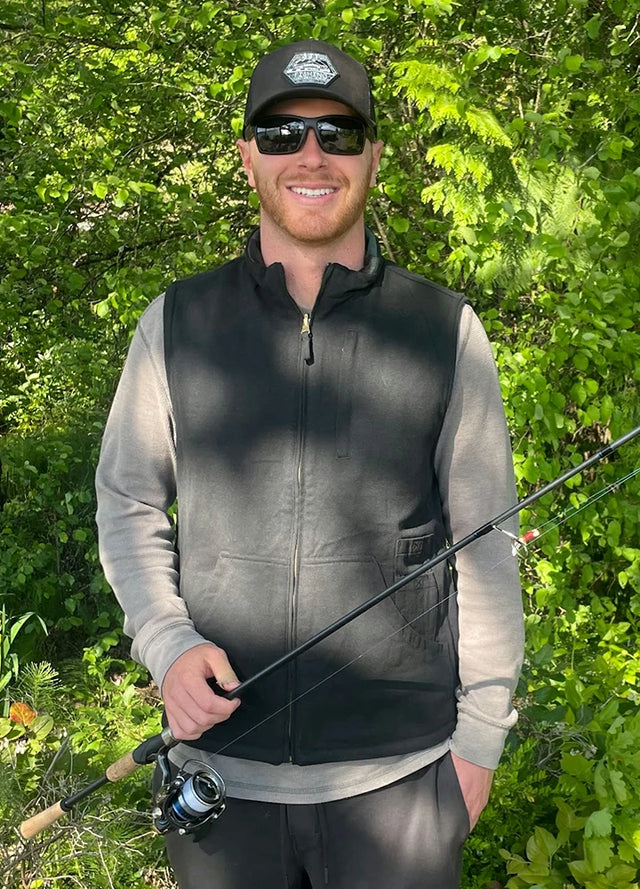 Front view of a man in a black green plaid men's reversible vest holding a fishing rod in his hand