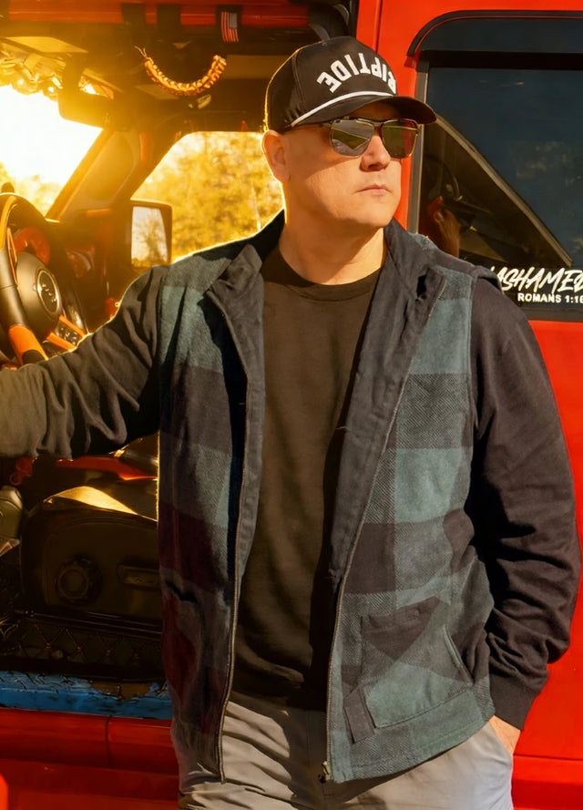 Front view of a man in a black green plaid men's reversible vest holding a fishing rod in his hand