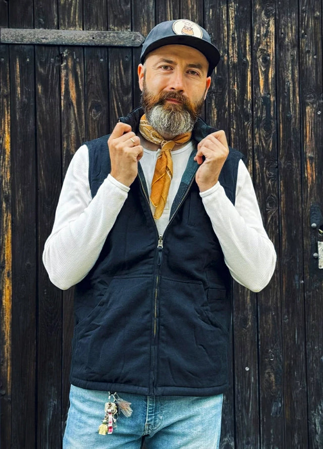 Front view of a man in a black green plaid men's reversible vest standing in front of the wall