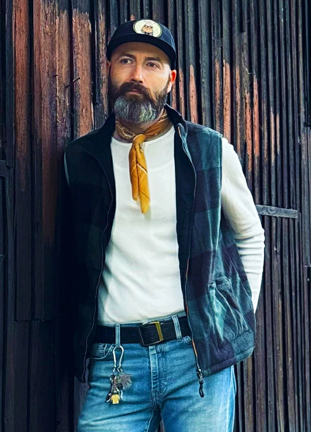 Front view of a man in a black green plaid men's reversible vest with his hands behind his back