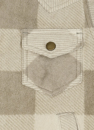 Close-up of a beige and off-white plaid fabric with a front pocket featuring a single round brass snap button.