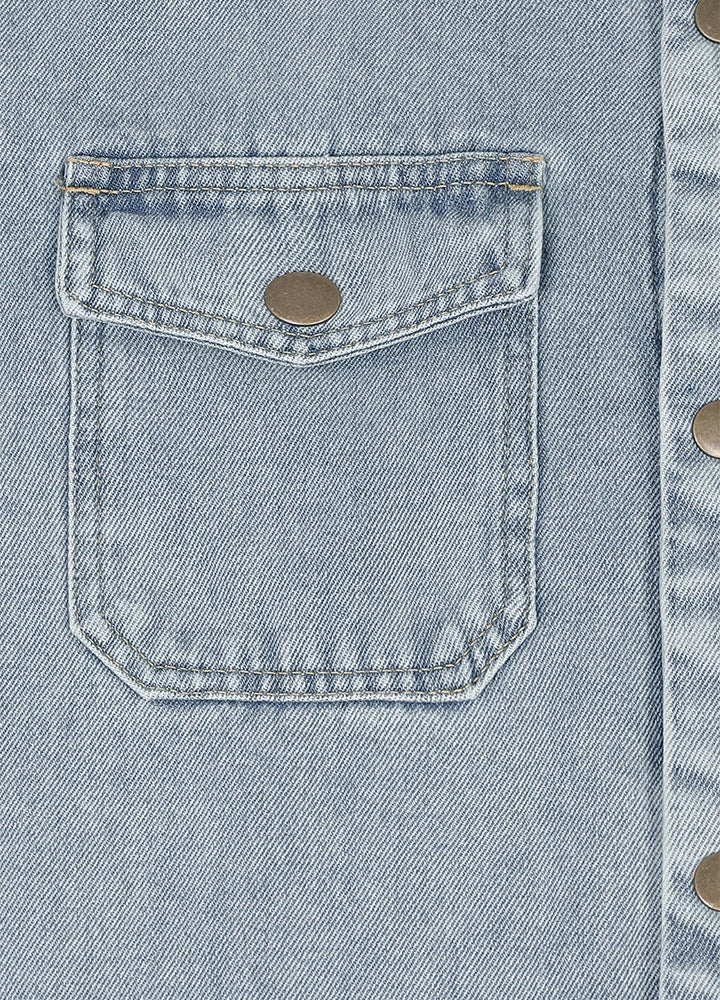 Close-up of a light blue denim jacket showing a front flap pocket with a metal snap button and part of the buttoned front closure.