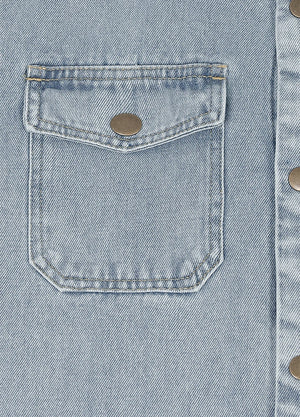 Close-up of a light blue denim jacket showing a front flap pocket with a metal snap button and part of the buttoned front closure.