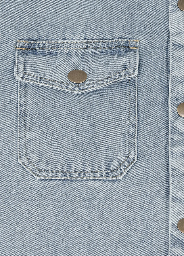 Close-up of a light blue denim jacket showing a front flap pocket with a metal snap button and part of the buttoned front closure.