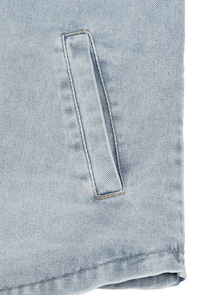 Close-up of a light blue denim garment showing a vertical welt pocket and folded hem on a white background.