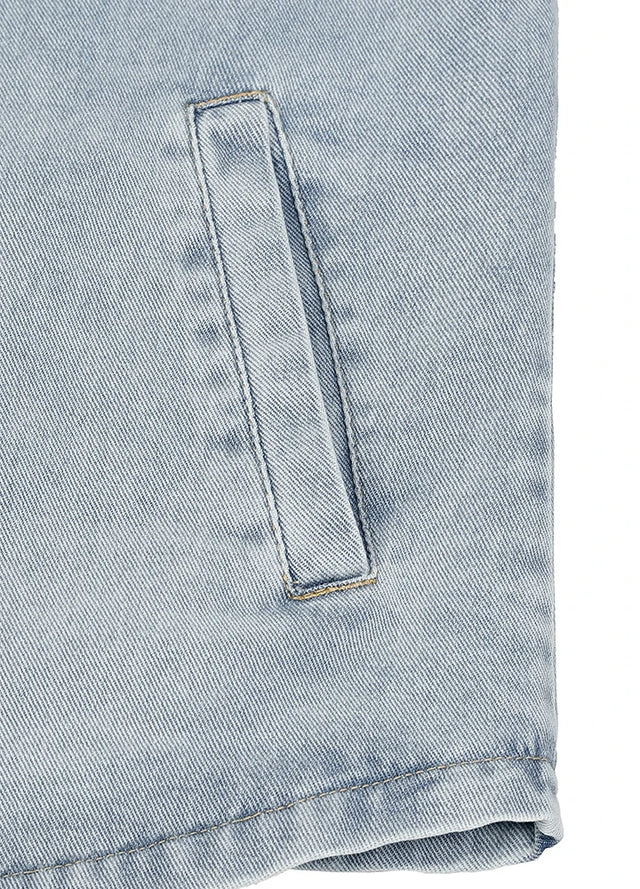 Close-up of a light blue denim garment showing a vertical welt pocket and folded hem on a white background.