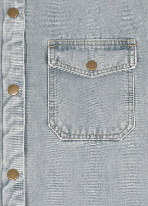 Close-up of a light blue denim button-up shirt featuring a chest pocket with a flap and a brass snap button.